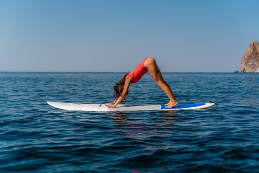 Sporty girl on a surfboard in the sea on a sunny summer day. In a red swimsuit, she sits in the splits on the sap. Summer entertainment on Stortom by the sea.