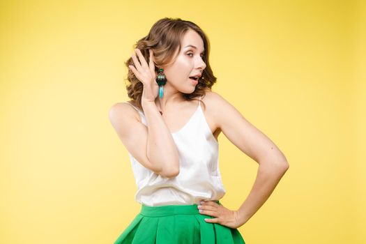 Studio portrait of curious brunette girl in multicolored top listening to the news or gossips with her ear.