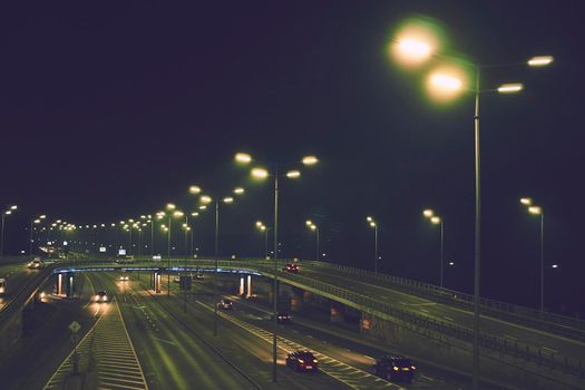 a broad road in a town or city, typically having trees at regular intervals along its sides .Night shining avenue and bridge with moving cars and lights