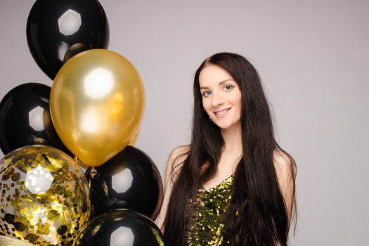Birthday photo session of attractive sexy model with long brunette hair in glitter party dress and high heels posing with golden and black air balloons. Isolate. Studio portrait.
