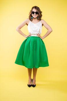 Summer outfit on orange background. Stylish and trendy beautiful young girl with wavy middle-length hair in white top and green bottom wearing trendy earrings and black sunglasses. She is smiling over orange background. Copyspace. Isolate.