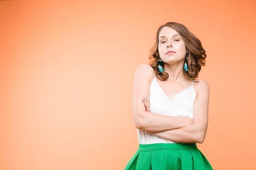 Studio portrait of unsatisfied young brunette caucasian woman with wavy hair in overall with colorful pattern holding arms folded and looking at camera with grief, dissatisfaction, anger and disbelief. Isolate.