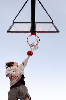 caucasian man playing in a basketball hoop seen from below with the sky in the background, concept of urban sport outdoors, copy space for text