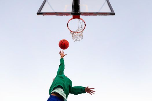 unrecognizable latin woman shooting in a basketball hoop seen from below with the sky in the background, concept of urban sport outdoors, copy space for text