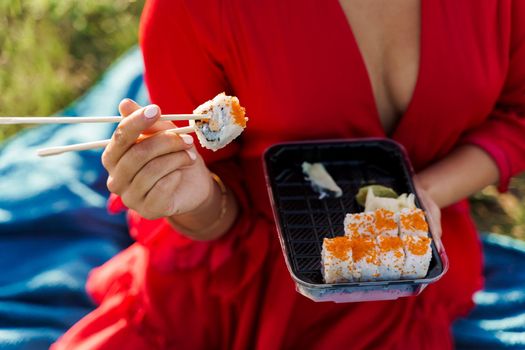 Close-up sushi set food delivery. Sexy girl holds sushi with chopsticks in hands. Courier delivered sushi set for pretty woman. Black box with sushi, wasabi, ginger.