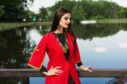 Georgian girl in red national dress with cross symbols. Attractive woman on the lake. Georgian culture lifestyle. Woman looks right side