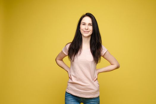 View from front of beautiful slim woman wearing white shirt and jeans standing steady on frey isolated background. Young blonde looking at camera, smiling and posing in studio.