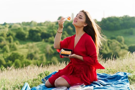 Sushi set and girl on green hills background. Food delivery service from japanese restaurant. Woman in red dress seats and eats sushi delivered by courier