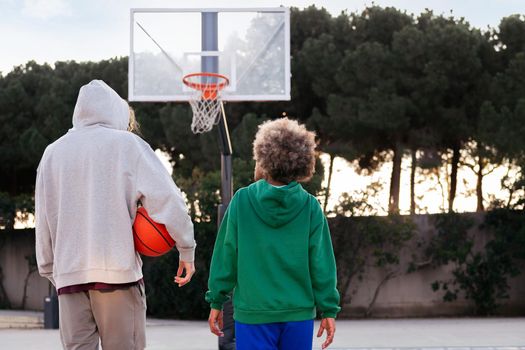 rear view of two friends walking on the basketball court after a game, concept of friendship and urban sport in the street, copy space for text