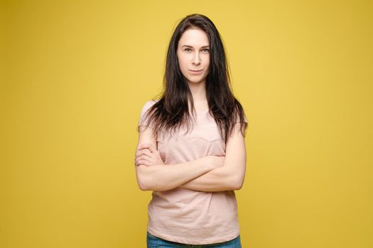 Studio portrait of fashionable brunette lady in white dress with flowers and beige heels posing with bent leg. Smiling at camera. holding skirt. Isolate on yellow background.