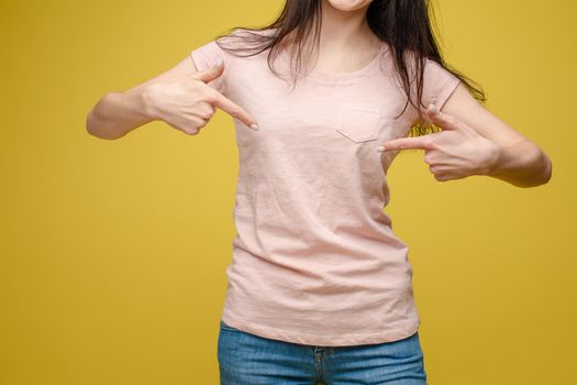 Cropped view from front of happy brunette standing in white shirt and jeans and pointing at outfit with fingers. Cheerful girl laughing and posing on grey isolated backround. Concept of casual style.