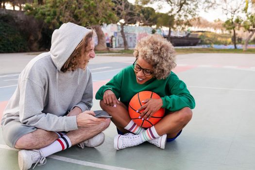 man and woman rest and have fun looking at the phone after basketball practice in a city park, concept of friendship and urban sport in the street, copy space for text