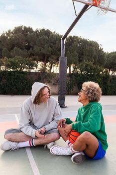 man and woman laughing and having fun with the phone after basketball practice in a city park, concept of friendship and urban sport in the street, copy space for text