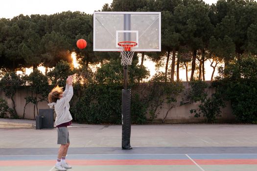 unrecognizable young caucasian man shooting baskets in a city park court, concept of urban sport outdoors