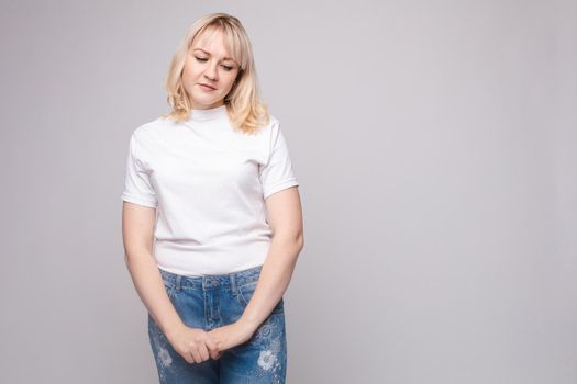 Upset young beautiful woman standing with crossed hands isolated at white studio background medium long shot. Unhappy European female looking down having negative emotion