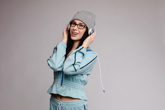 Happy brunette wearing blue tracksuit jumping and laughing on grey isolated background. Young cheerful woman with long hair having fun and posing in studio. Concept of happiness and motion.