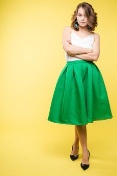 Studio portrait of unsatisfied young brunette caucasian woman with wavy hair in overall with colorful pattern holding arms folded and looking at camera with grief, dissatisfaction, anger and disbelief. Isolate.