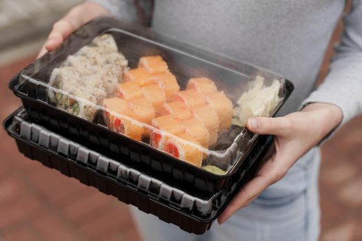 Closeup sushi set in box healthy food delivery online service. Girl holds 2 sushi sets in hands. Japanese cuisine: rolls, soy sauce, wasabi.