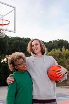 latin woman and caucasian man smiling happy after playing on a city park basketball court, concept of friendship and urban sport in the street, copy space for text