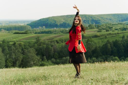 Georgian girl dances national dance in red national dress on the green hills of Georgia background. Georgian culture lifestyle.