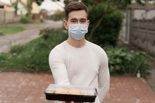 Sushi set in box healthy food delivery online service by car. Handsome man courier in medical mask gives sushi box to you. Japanese cuisine