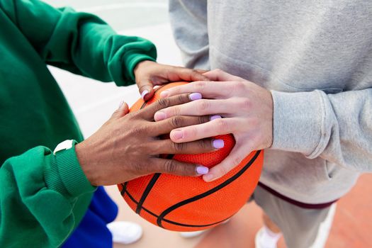 joined hands of a caucasian man and a latin woman over a basketball, concept of friendship and urban sport in the street, copy space for text