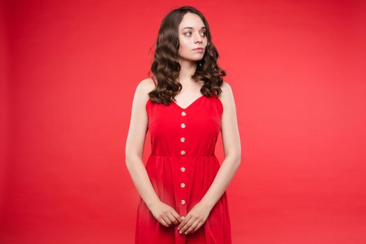 Front view of pretty brunette wearing red dress looking at camera while sparkles falling around in studio. Beautiful woman with hairstyle posing on isolated background. Concept of holiday.