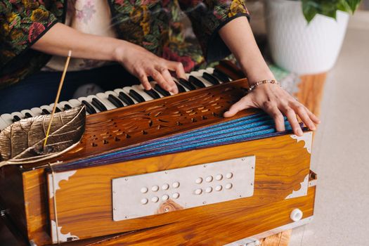 Hands of a woman sitting on the floor and playing the harmonium during the practice of kundalini yoga.