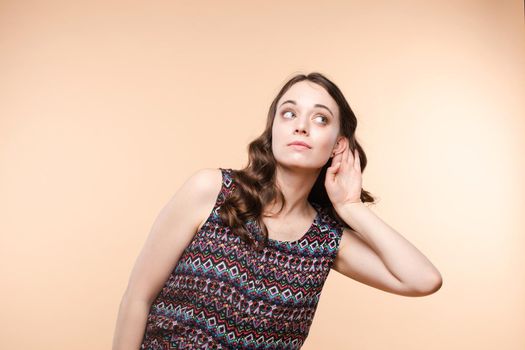 Studio portrait of curious brunette girl in multicolored top listening to the news or gossips with her ear.