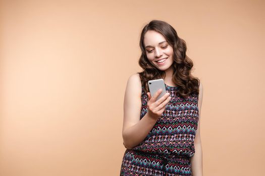 Studio portrait of beautiful caucasian brunette woman in patterned overall pointing at her smartphone with index finger. She is certain or sure about something. I know gesture.
