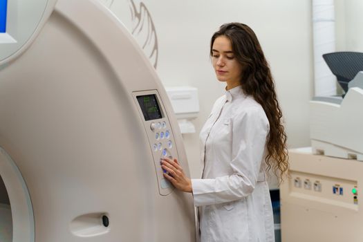 Medical student does practice with computer tomography. Young girl in white coat presses button on CT