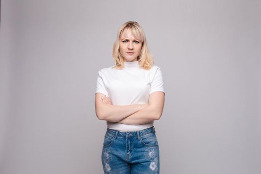 Studio portrait of unsatisfied young brunette caucasian woman with wavy hair in overall with colorful pattern holding arms folded and looking at camera with grief, dissatisfaction, anger and disbelief. Isolate.