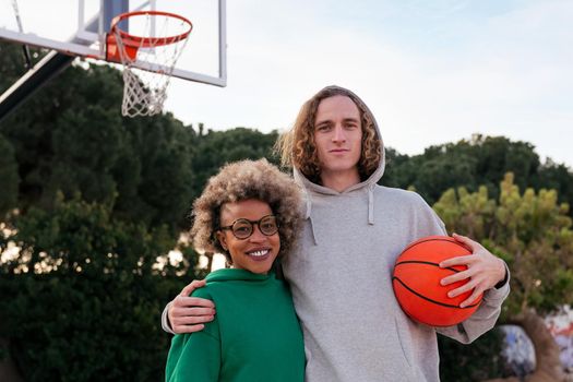 latin woman and caucasian man pose smiling on the basketball court in a city park, concept of friendship and urban sport