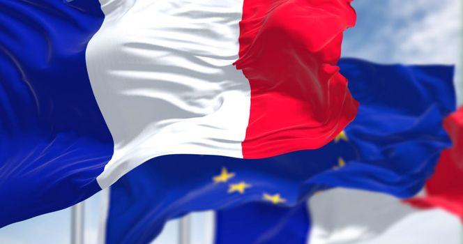 Detail of the national flag of France waving in the wind with blurred european union flag in the background on a clear day. Democracy and politics. European country. Selective focus.