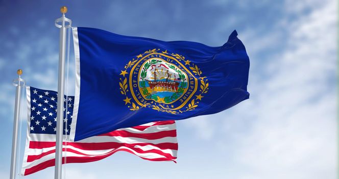 The New Hampshire state flag waving along with the national flag of the United States of America. In the background there is a clear sky. New Hampshire is a state in the New England region of the US