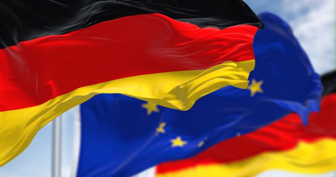 Detail of the national flag of Germany waving in the wind with blurred european union flag in the background on a clear day. Democracy and politics. European country. Selective focus.