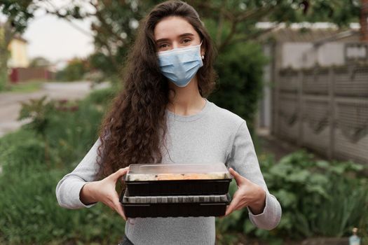 Girl courier in medical mask with 2 sushi boxes stands in front of car. Sushi set in box healthy food delivery service by car