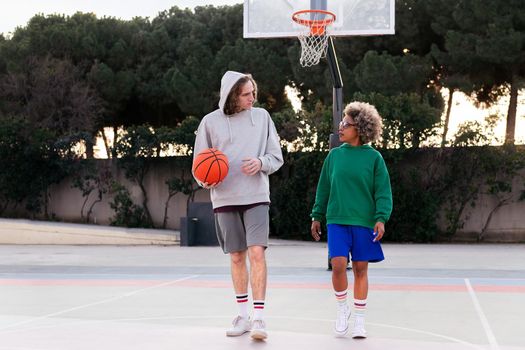 latin woman and caucasian man chatting while walking on the basketball court after a game, concept of friendship and urban sport in the street, copy space for text