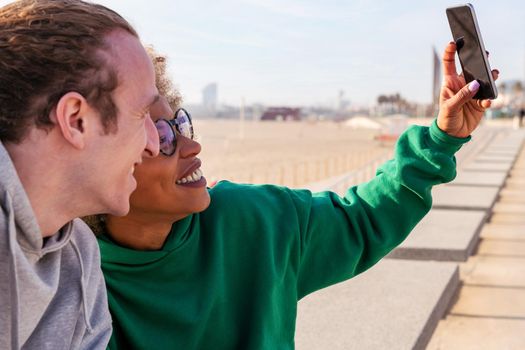 young latin woman smiling with her friend while taking a selfie photo with the mobile phone, concept of lifestyle and friendship