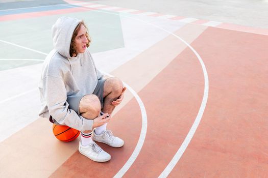 surprised caucasian man sitting on the court after basketball practice, concept of urban sport outdoors, copy space for text