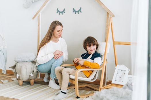 Happy caucasian mother sitting with son in children's room, looking at tablet computer device. Smiling family plays video games with kid boy together. Mom and chilld wathcing on touch screen.