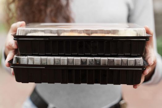 Close-up sushi in box healthy food delivery online service. Girl holds 2 sushi sets in hands. Japanese cuisine: rolls, soy sauce, wasabi