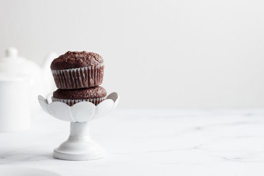 Chocolate muffins in a white cake stand on a white table