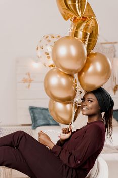 Muslim black girl with golden helium balloons smiles. African young woman celebrates her birthday