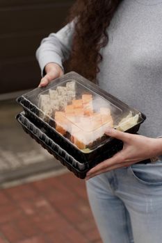 Close-up sushi in box healthy food delivery online service. Girl holds 2 sushi sets in hands. Japanese cuisine: rolls, soy sauce, wasabi