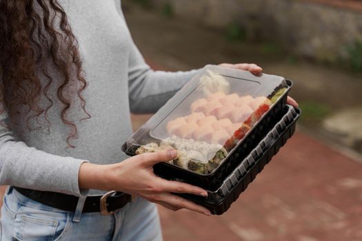 Close-up sushi in box healthy food delivery online service. Girl holds 2 sushi sets in hands. Japanese cuisine: rolls, soy sauce, wasabi