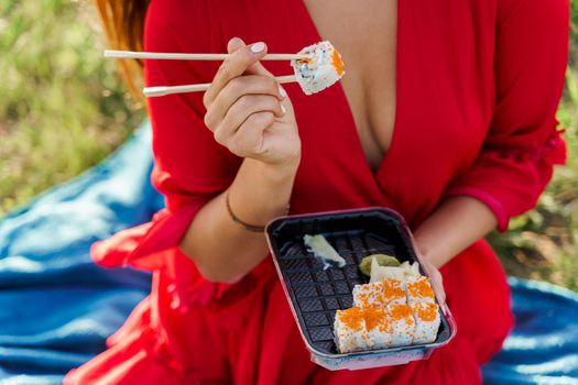 Close-up sushi set food delivery. Sexy girl holds sushi with chopsticks in hands. Courier delivered sushi set for pretty woman. Black box with sushi, wasabi, ginger.