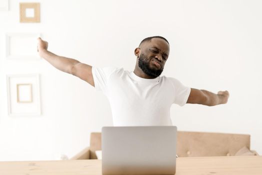 African American man working on laptop suffers from back pain, sprains his back after long time working on laptop at home