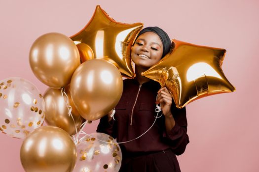 Christmas celebration. African american holiday. Attractive girl with golden helium balloons isolated peach background