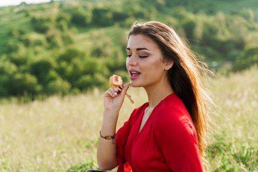 Sushi set and girl who reach out to bite sushi on green hills background. Food delivery service from japanese restaurant. Woman with blue eyes in red dress seats and eats sushi delivered by courier